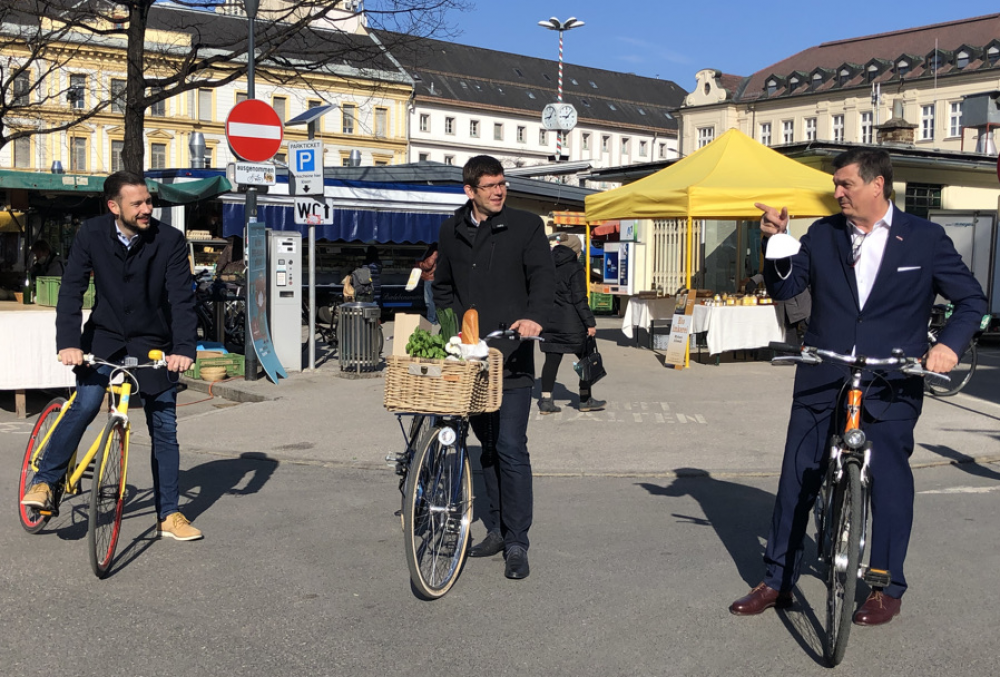 Drei Personen auf Citybikes vor einem Marktplatz